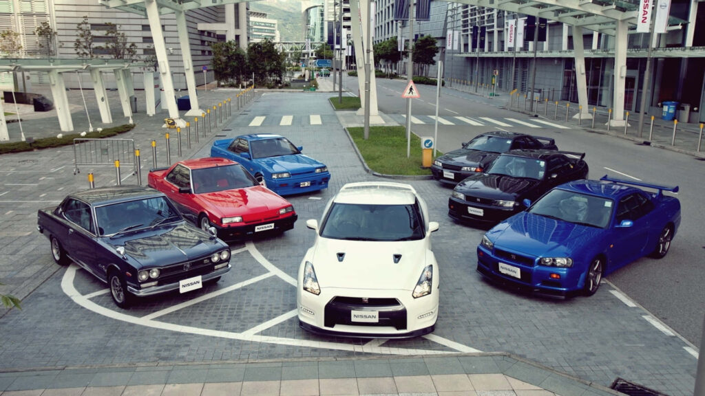 Lineup of Nissan Skyline GT-R models including multiple R33 GT-Rs in vibrant colors urban setting Wallpaper