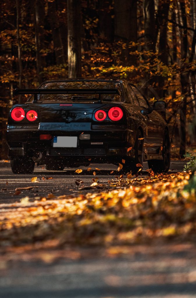 Nissan Skyline GT-R R34 black JDM car driving on autumn forest road with glowing taillights Wallpaper