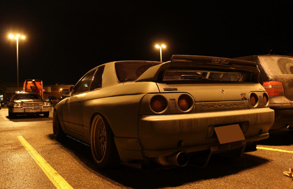Nissan Skyline rear view at night with custom rims dusty finish and rear spoiler in parking lot Wallpaper