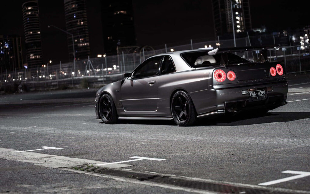 Nissan Skyline R34 parked under city lights on empty urban street night street racing wallpaper