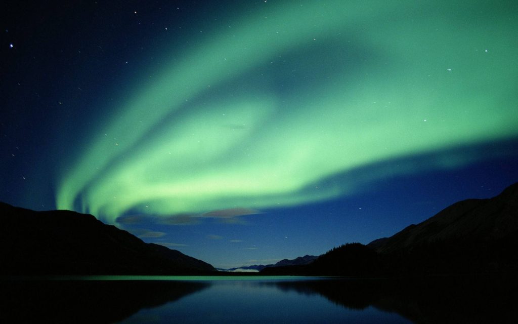 Northern Lights vibrant green aurora borealis over calm water and dark mountain silhouettes wallpaper