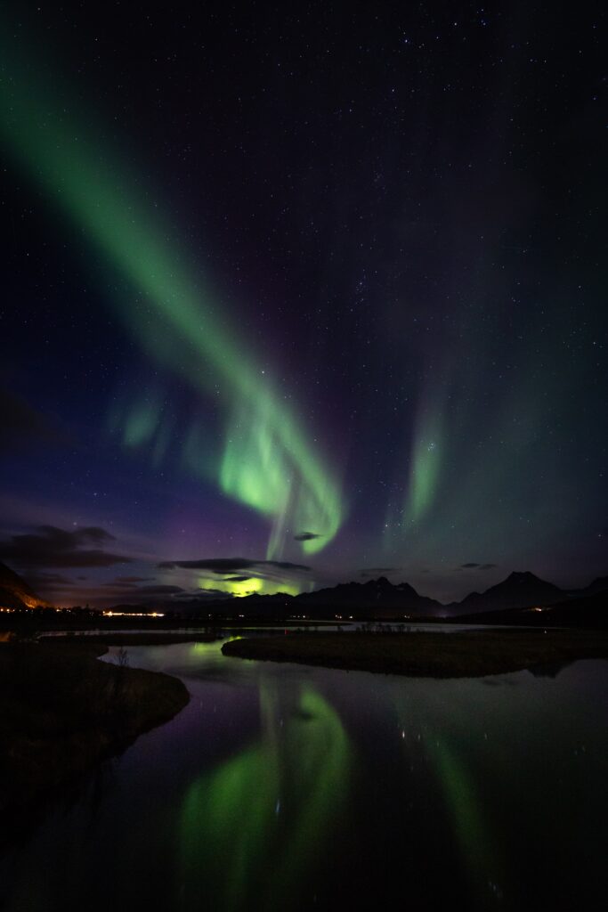 Northern lights in green and purple over rugged mountains reflecting in a calm river at night Wallpaper