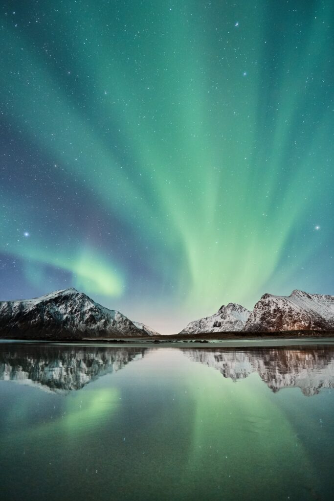Northern lights over snow-capped Lofoten Islands with green auroras reflecting on icy waters Wallpaper