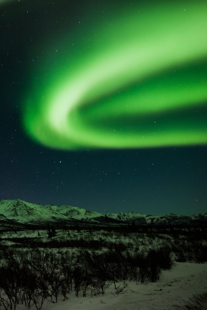 Northern lights green waves over starry sky and snow-covered mountains wallpaper background