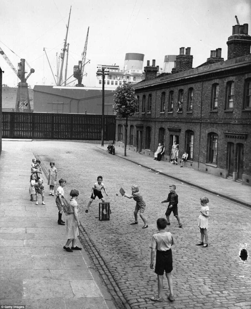 Children Playing Cricket: Nostalgic Black-and-White Street Scene Wallpaper