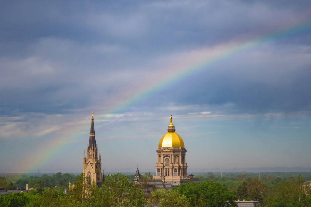 University of Notre Dame Golden Dome Basilica steeple rainbow cloudy sky green trees wallpaper