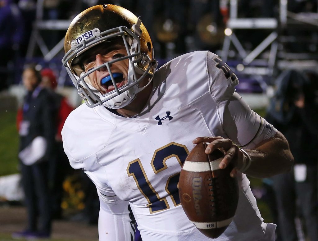 Notre Dame quarterback Ian Book in white jersey and gold helmet during intense night game action Wallpaper