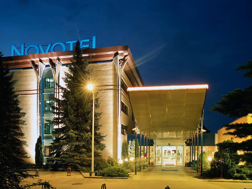 Novotel hotel exterior at night glowing blue sign modern design lush greenery twilight sky Wallpaper