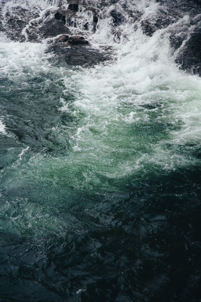 Ocean waves crashing on dark rocks with vivid blue green foam in high resolution wallpaper