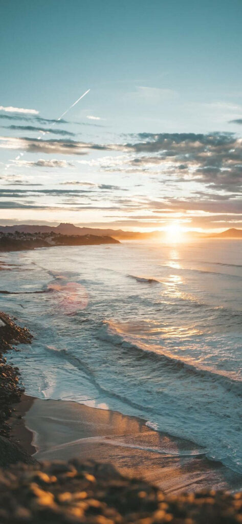 Serene ocean sunset iPhone wallpaper with gentle waves and glowing golden sky on beach