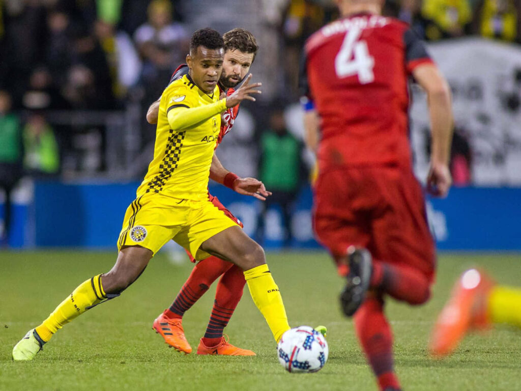 Ola Kamara Columbus Crew in yellow kit shielding ball from Toronto FC defender red jersey intense soccer match Wallpaper