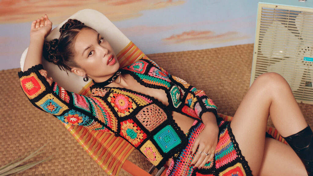 Olivia Rodrigo: Confident Crochet Outfit in Artistic Wallpaper Background
