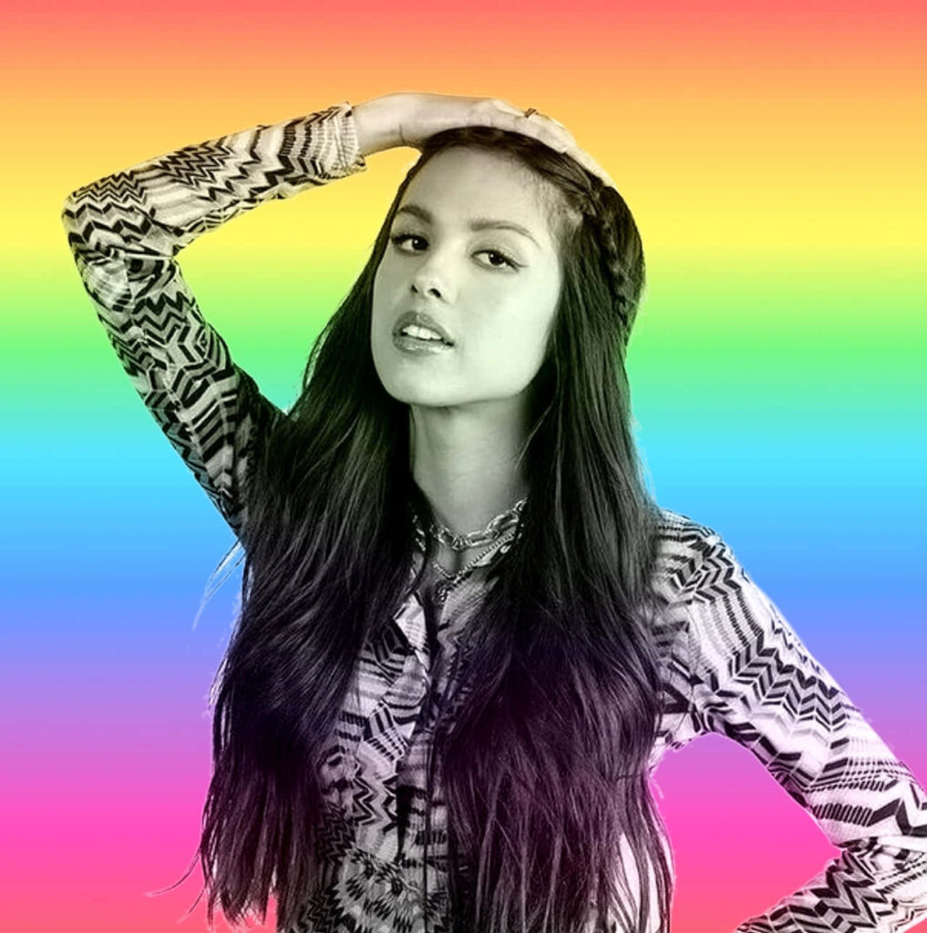 Olivia Rodrigo Stylish Wallpaper: Confident Pose & Rainbow Background