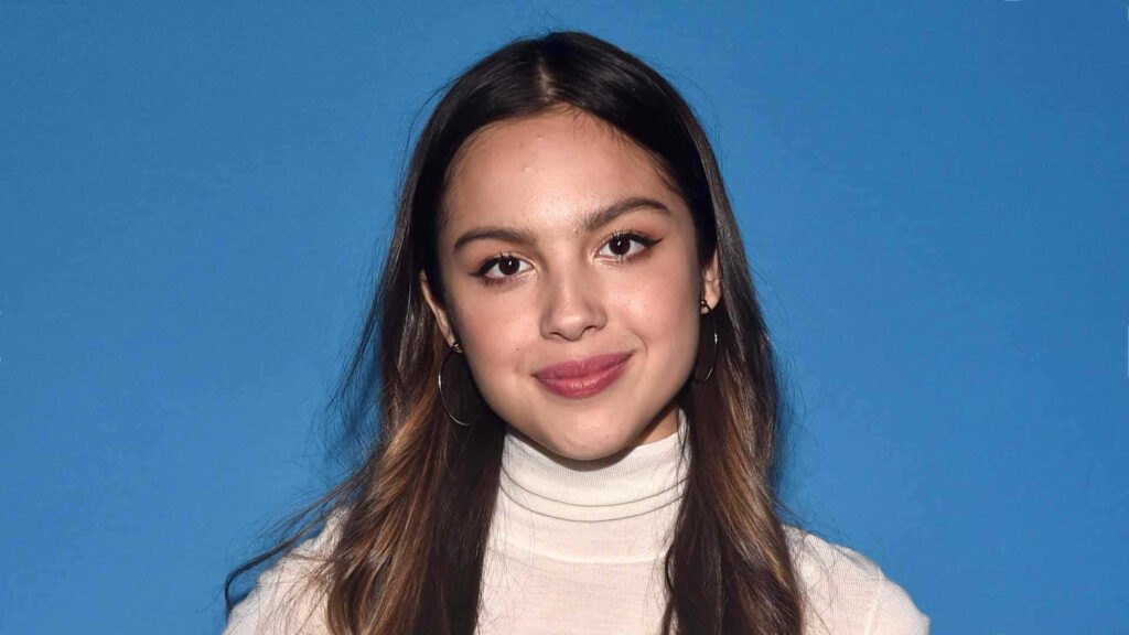 Olivia Rodrigo Wallpaper: Confident Charm on Vibrant Blue Background