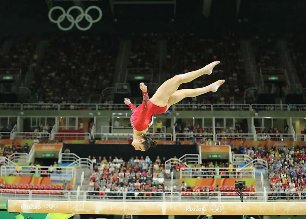 Dynamic Gymnastics Wallpaper: Olympic Mid-Air Flip on Balance Beam