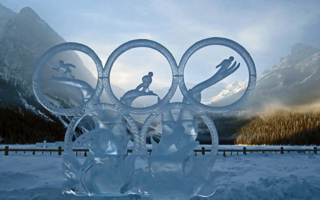 Olympic rings ice sculpture with winter athletes carved ice mountain snow background wallpaper