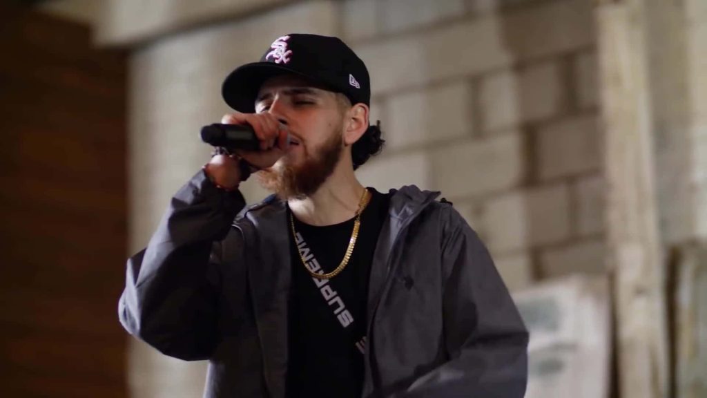 Omar Ruiz live performance singing in Supreme and White Sox cap with blurred brick wall background Wallpaper