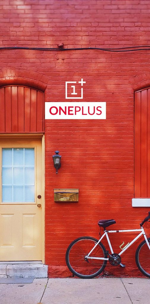 OnePlus wallpaper with logo on red brick house featuring yellow door mailbox and bicycle urban style