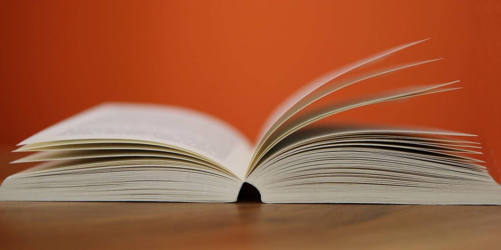Open book on wooden table with vibrant orange background education wallpaper for study focus