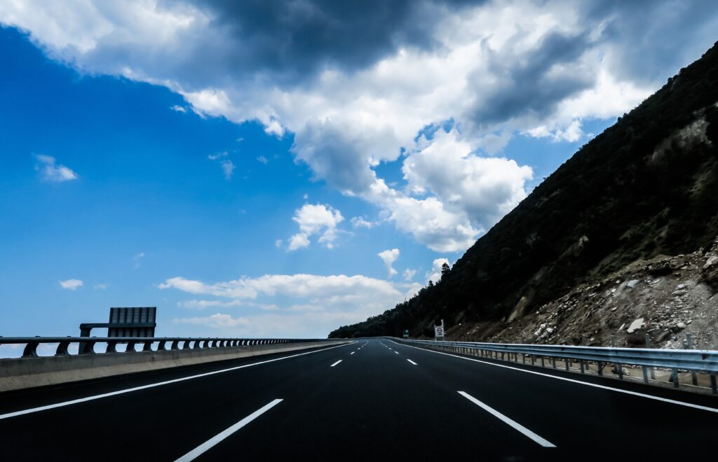 Open road with white markings leading to mountains under a bright blue cloudy sky wallpaper background