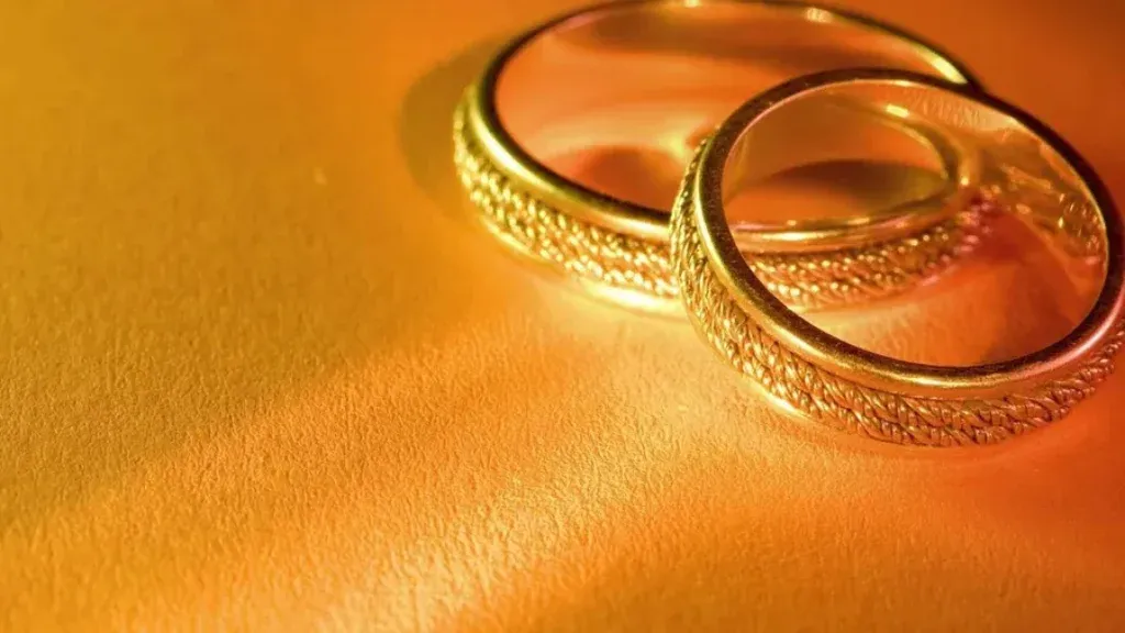 Opulent Overlapping Diagonals: Luxurious Golden Wedding Rings on Vibrant Orange Surface Wallpaper