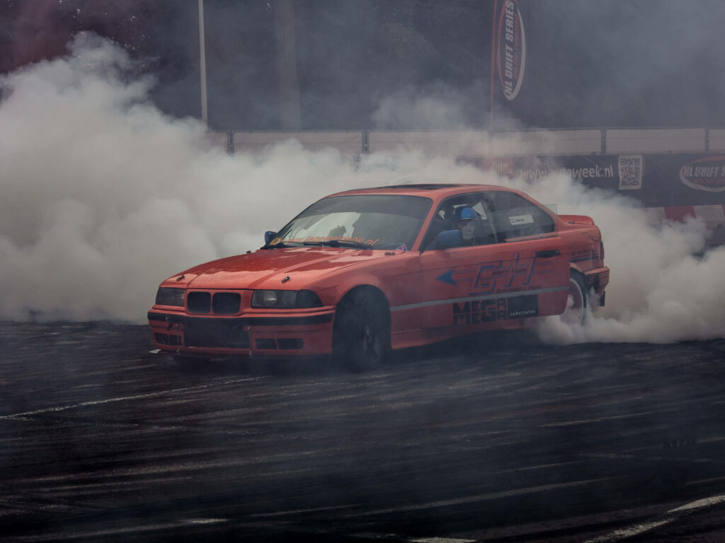 Orange BMW E36 drifting on track with thick smoke showcasing power and precision wallpaper