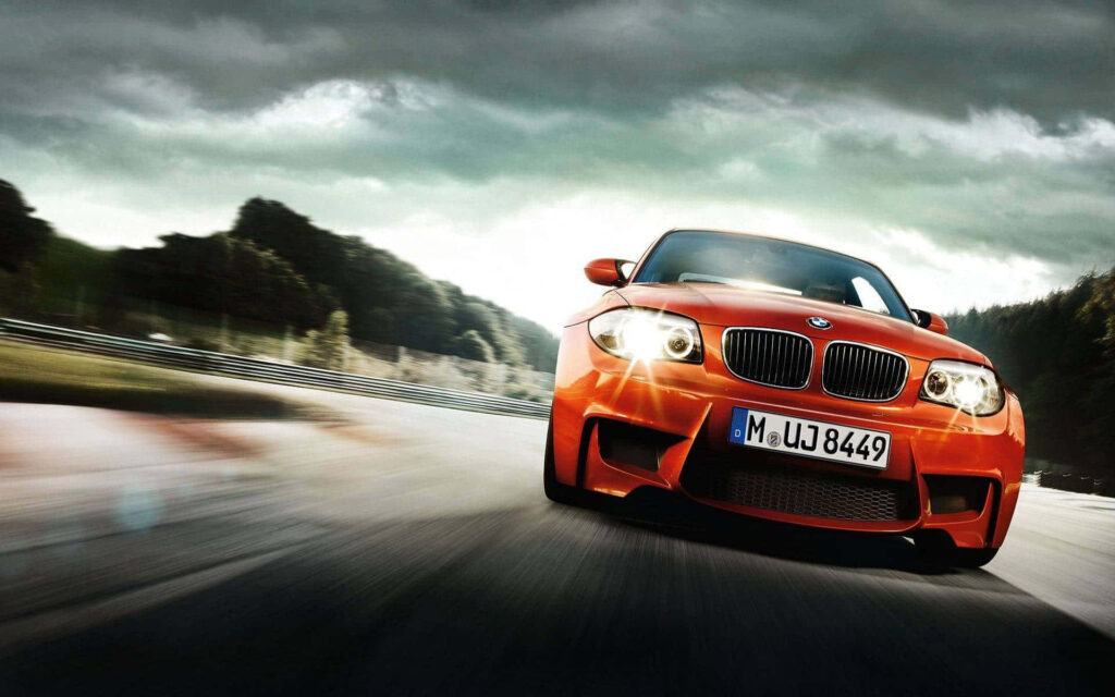 Orange BMW M1 racing fast on track with dramatic clouds iconic sports car wallpaper background