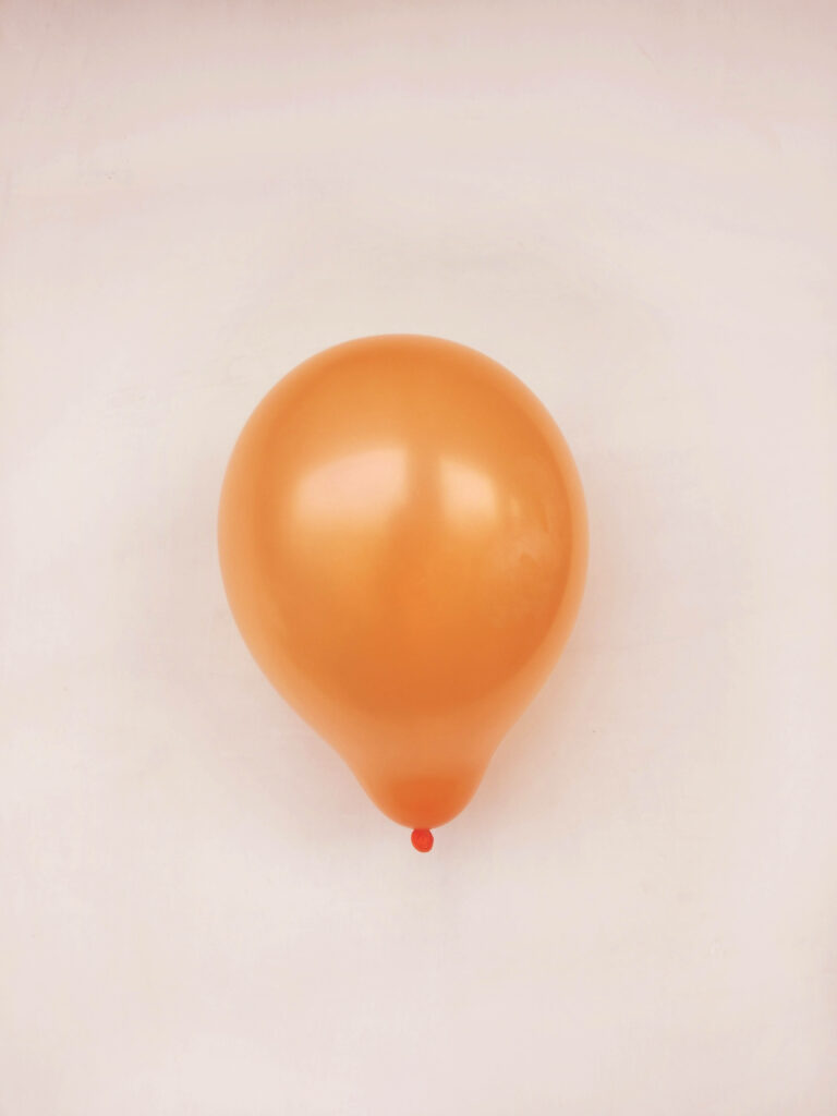 Single orange balloon floating on soft beige background simple cheerful wallpaper design