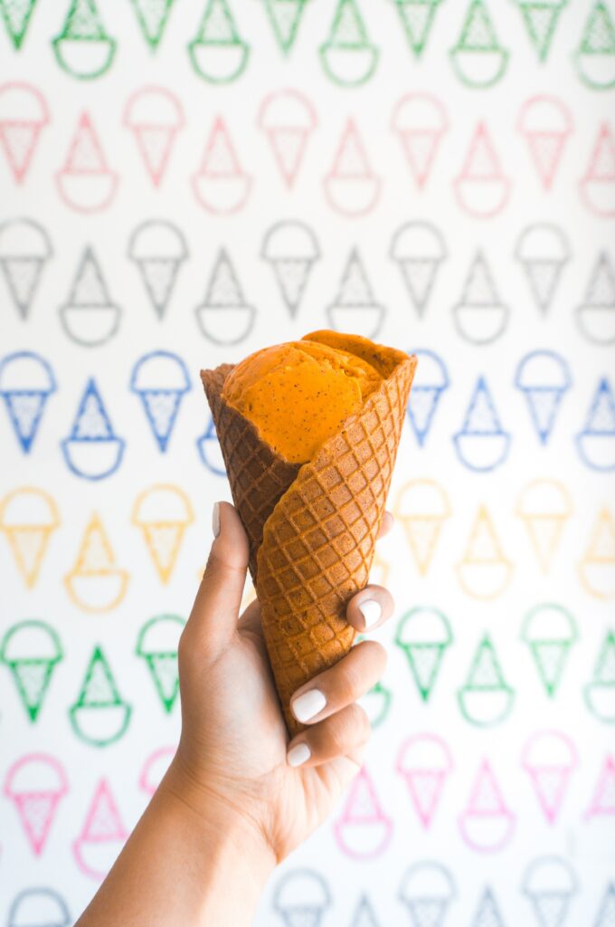 Colorful Wallpaper: Hand Holding Waffle Cone with Orange Ice Cream