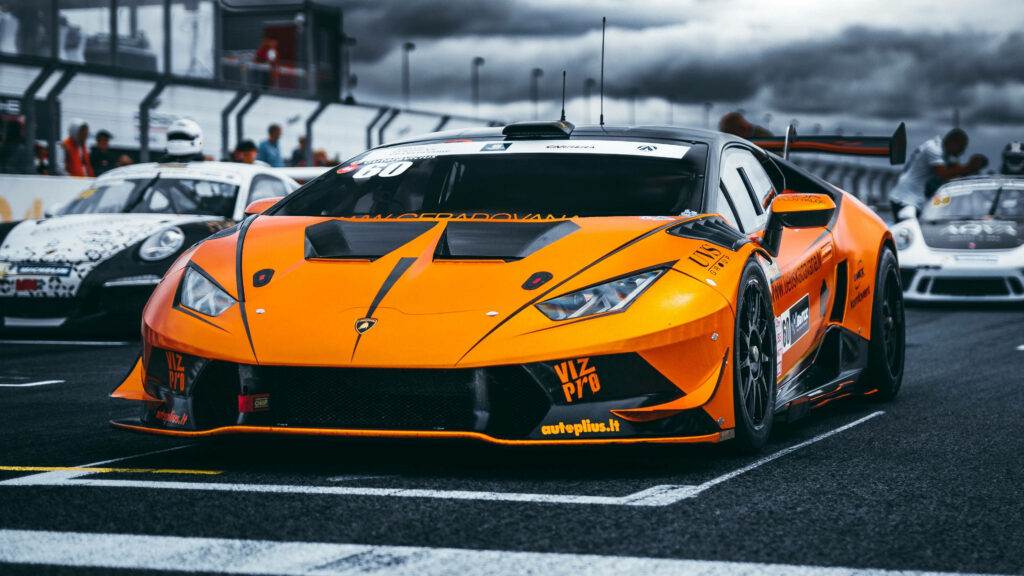 Orange Lamborghini race car contrasts with white cars on racetrack under dramatic cloudy sky 4K Wallpaper