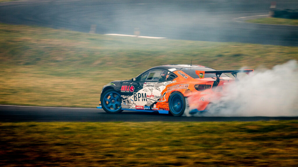 Orange sports car drifting on racetrack with smoke trailing high speed turn wallpaper background