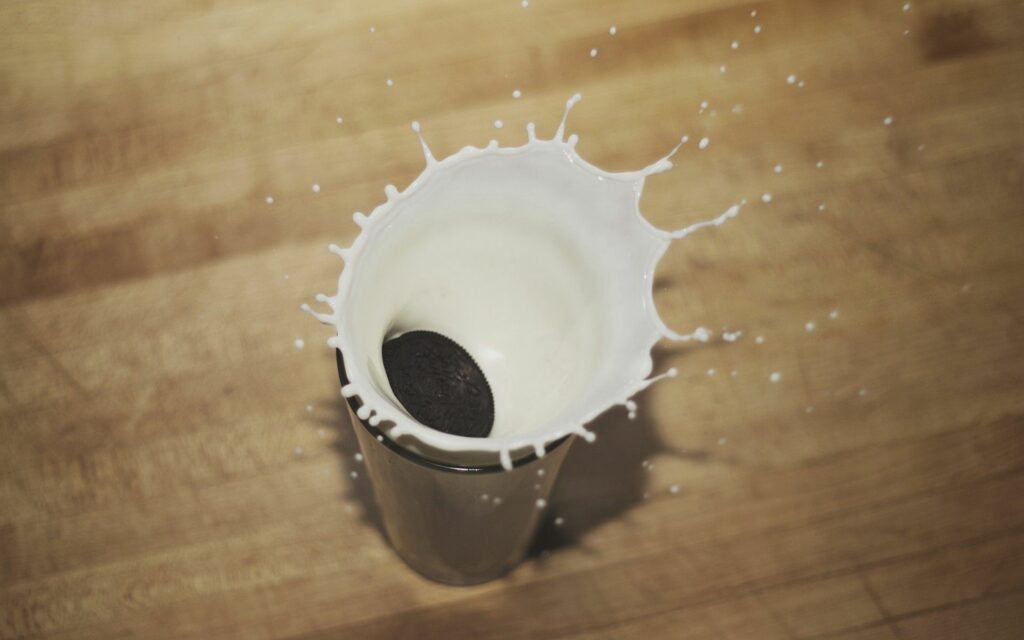 Dynamic Splash: Oreo Drops into Milk on Rustic Wooden Surface Wallpaper