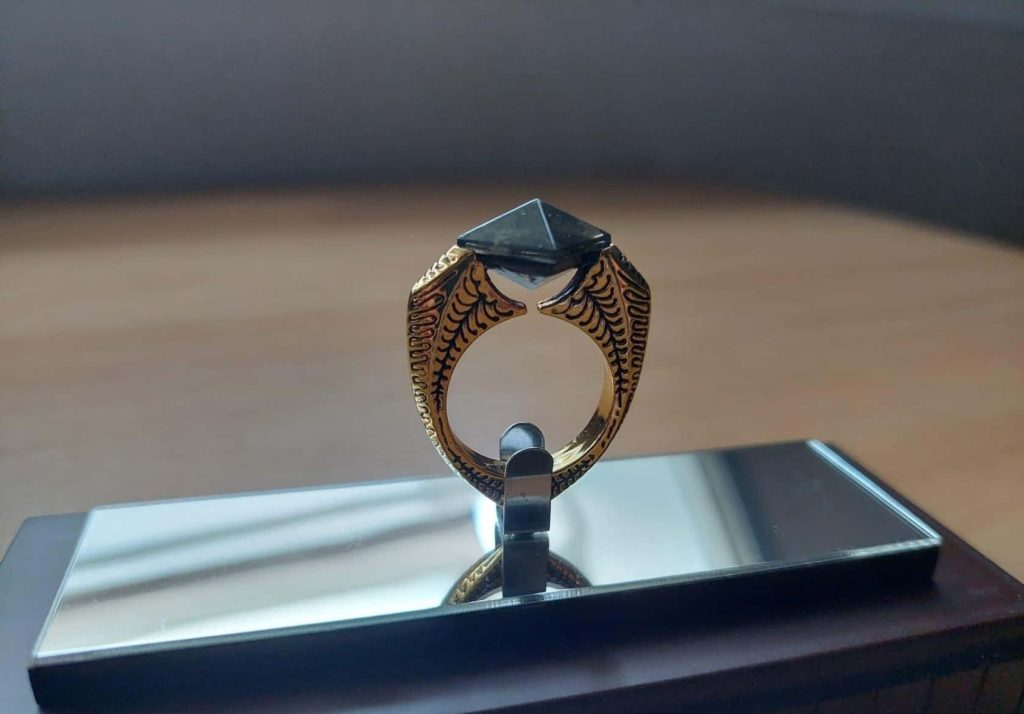 Macro shot of ornate golden ring with pyramid black stone on mirrored stand fantasy wallpaper background
