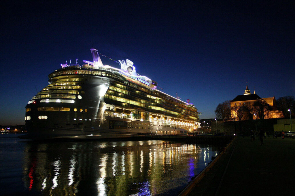Grand cruise ship lit with colorful lights docked at Oslo waterfront at night with reflections Wallpaper