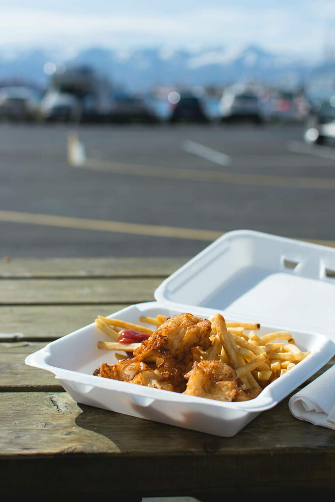 Crispy Fish and Golden Fries in Styrofoam on Outdoor Wooden Table Wallpaper