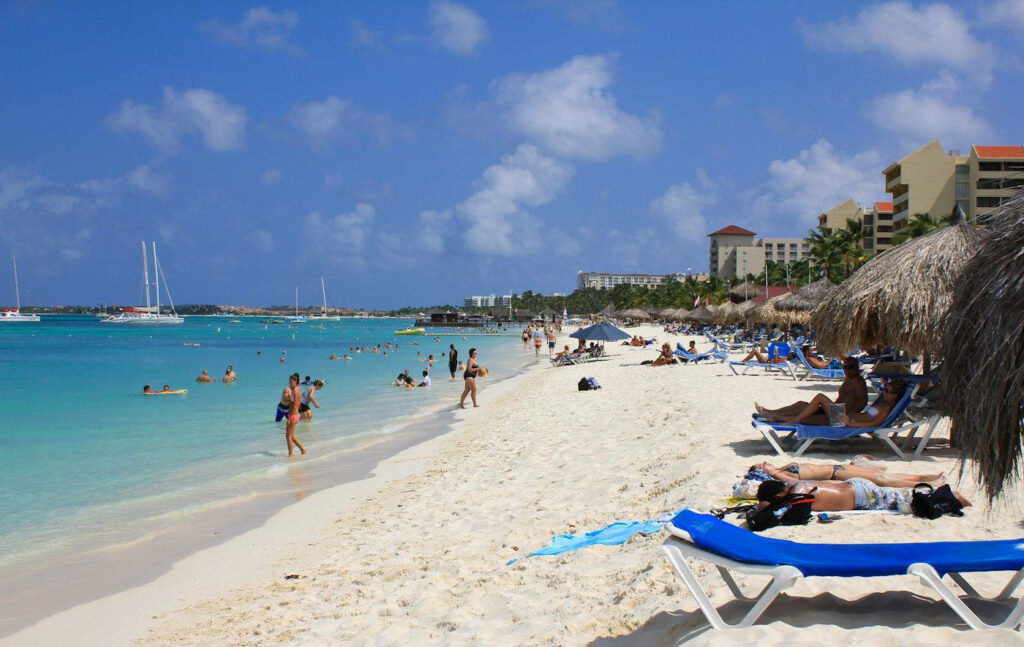 Paradise Found: Captivating View of Tourists Relishing Palm Beach's Pristine White Sands - Aruba Background Snapshot Wallpaper