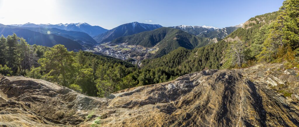 Panoramic mountain landscape with rocky slopes green trees snowy peaks and vibrant blue sky wallpaper