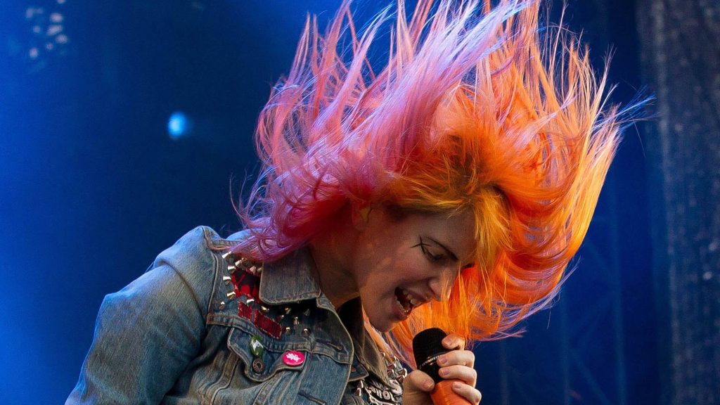 Hayley Williams of Paramore mid-headbang live performance orange pink hair blue stage light Wallpaper
