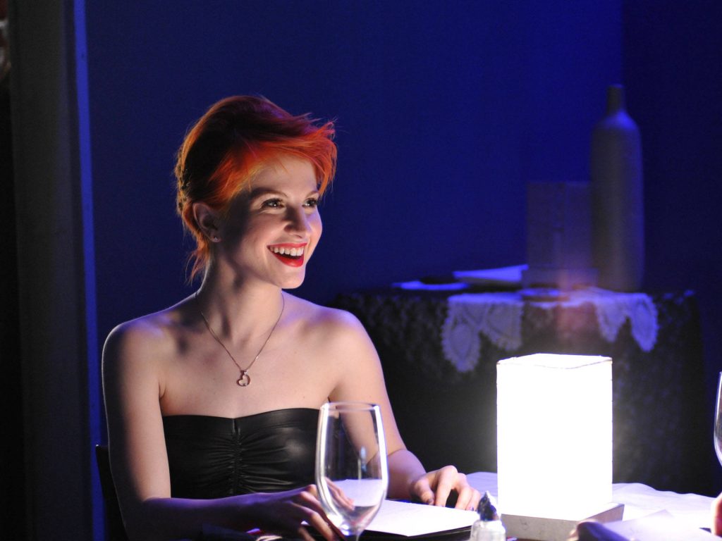 Hayley Williams from Paramore smiling in black top with orange hair and warm lamp light background Wallpaper