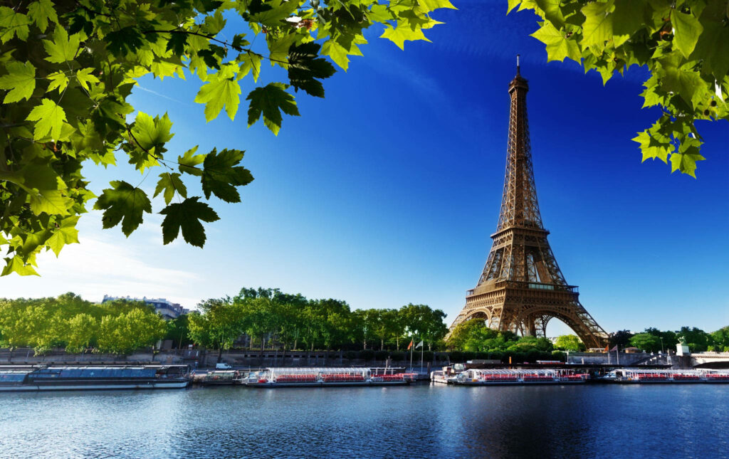 Eiffel Tower with green leaves boats on River Seine sunny blue sky Paris wallpaper background