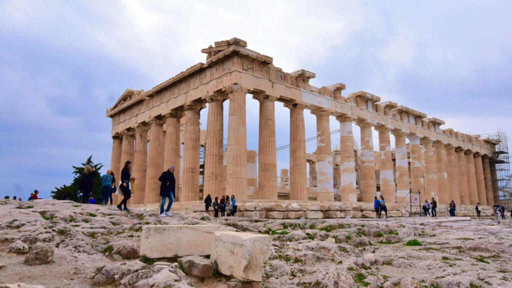 Parthenon ruins in Athens with visitors exploring iconic marble columns under dramatic sky background Wallpaper