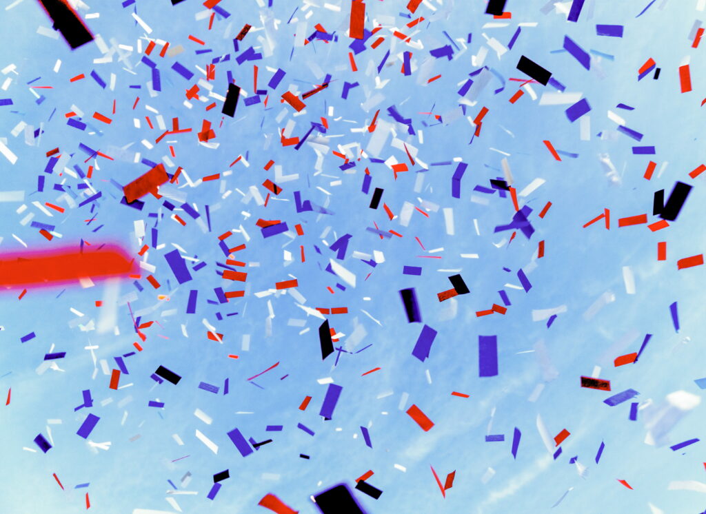 Festive confetti in red blue black white falling on bright blue sky vibrant celebration background Wallpaper
