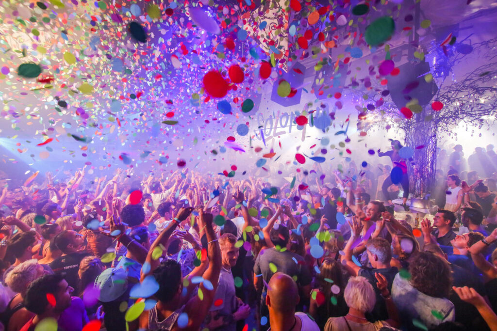 Happiness Unleashed: Party-goers in Ibiza Revel Under a Rain of Vibrant Confetti amid a Lively Crowd Wallpaper