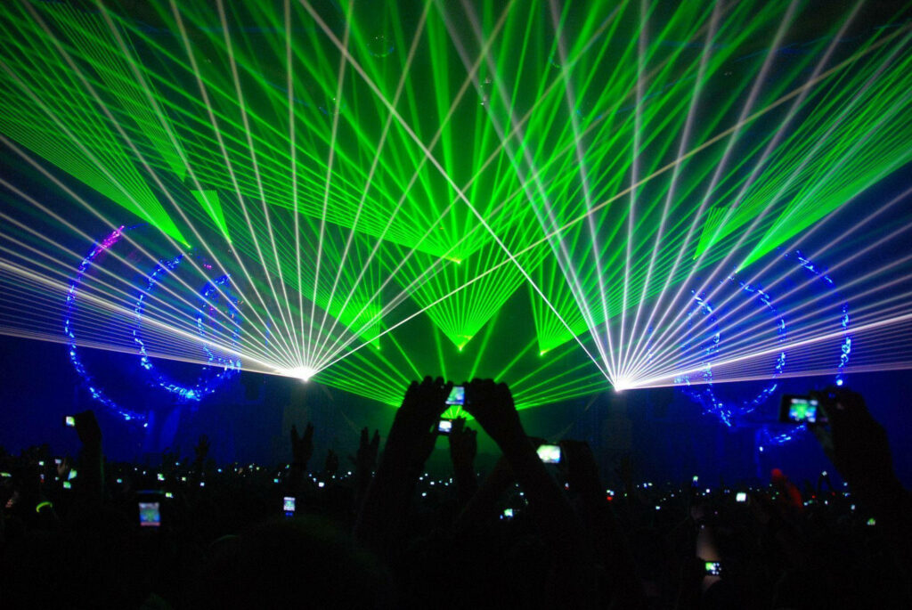 Concert crowd lit by vibrant green lasers and bright white lights at an EDM festival wallpaper