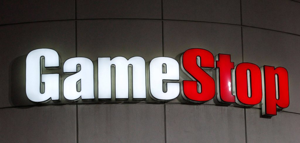 Night photo of illuminated GameStop sign with bright white and red letters on grey wall Wallpaper
