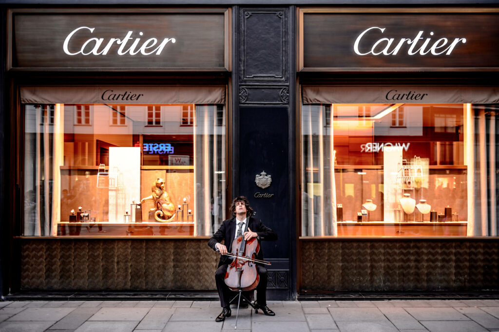 Passionate cellist performing on Vienna streets by luxury Cartier store showcasing culture Wallpaper