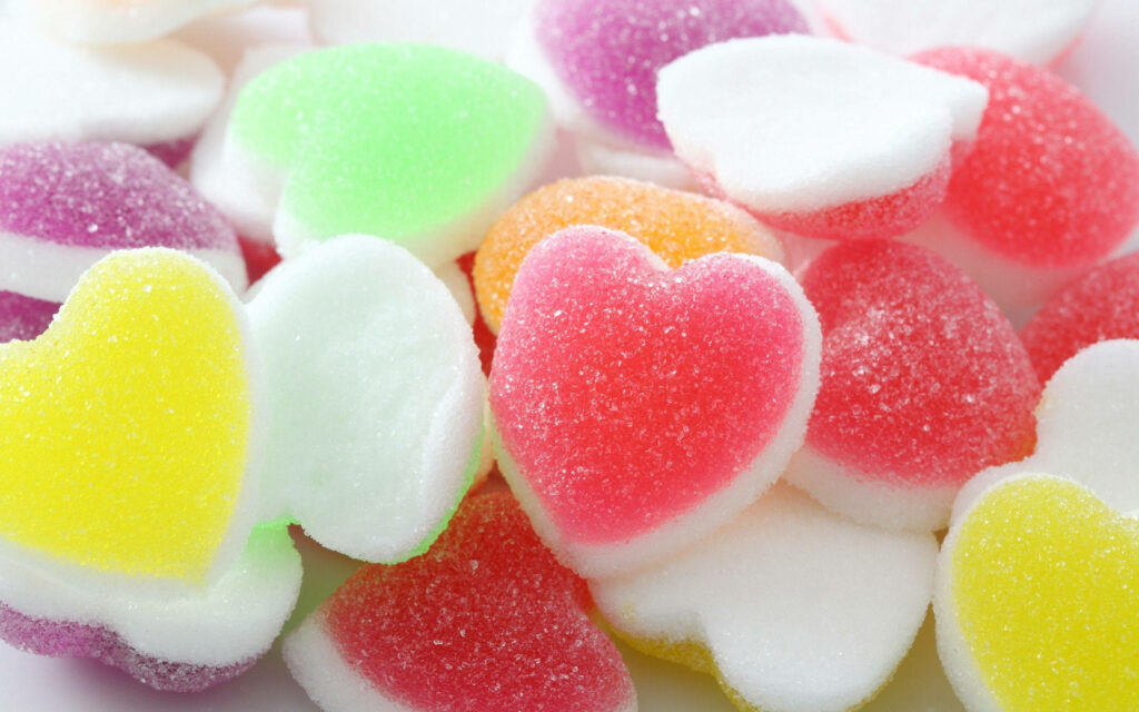 Colorful pastel heart-shaped gummy candies with sugary coating creating a playful wallpaper