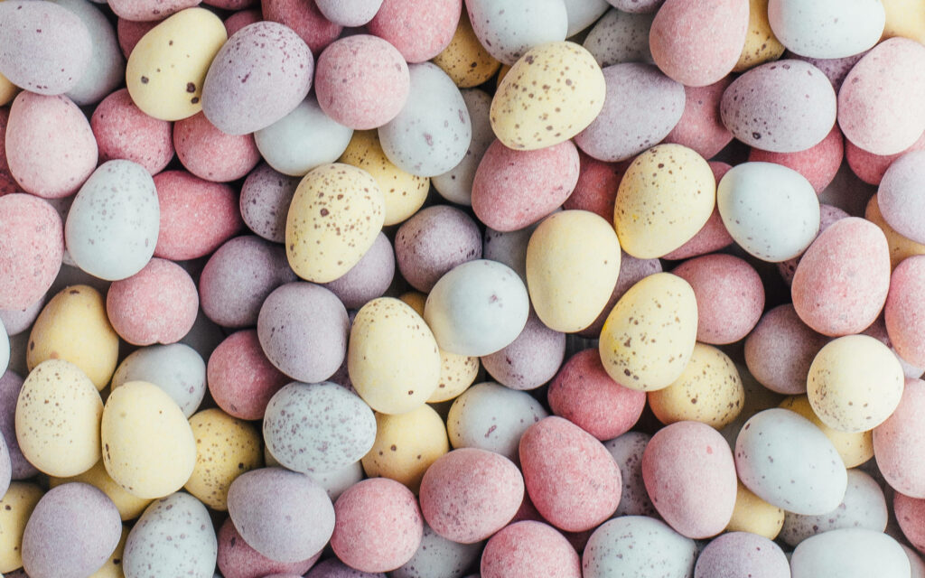 Pastel speckled chocolate mini eggs flat lay wallpaper in soft pink yellow blue for calming background