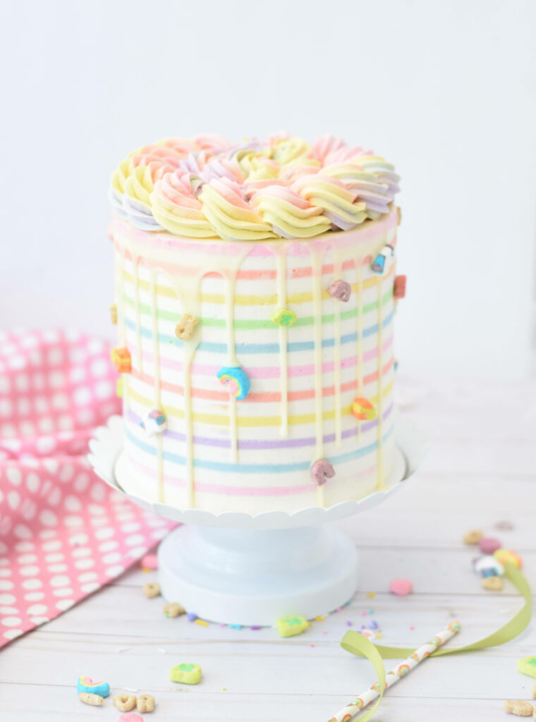 Pastel rainbow layer cake with frosting swirls and candy on bright cheerful wallpaper background
