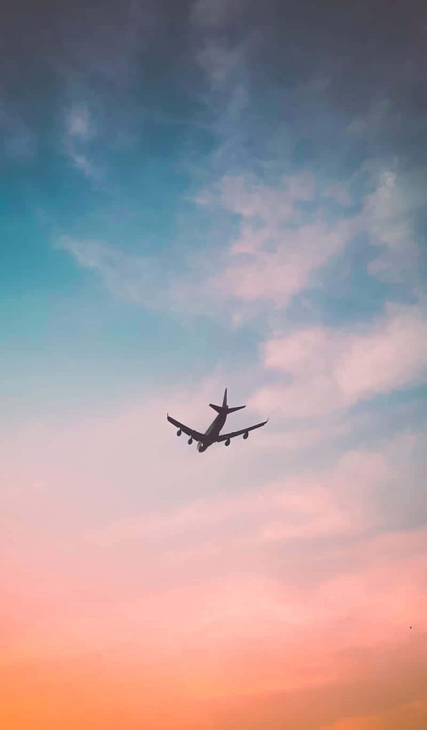 Silhouette of quad-engine passenger jet flying through pastel orange to blue sky background wallpaper